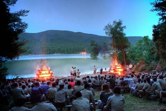a bonfile near a lake with dozens of people in an amphitheater