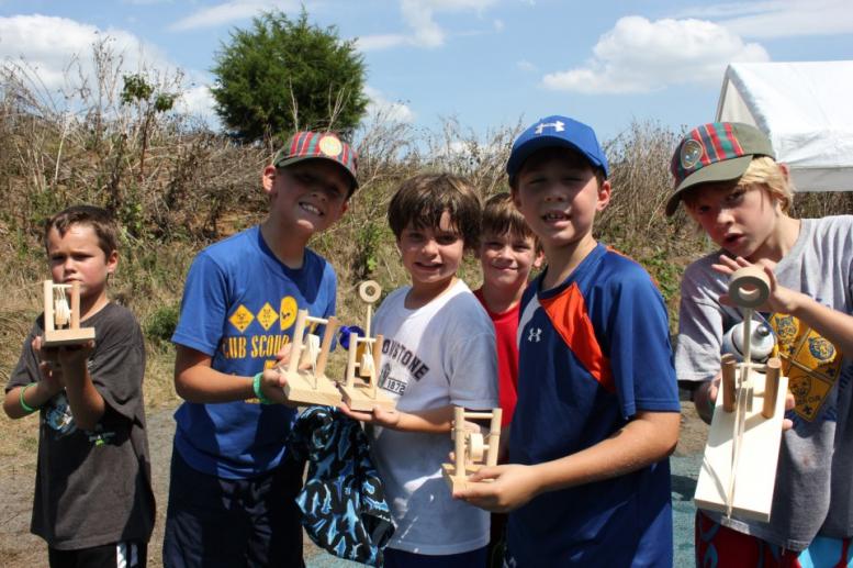 a group photo of cub scouts showing off their wooden catapult projects at summer camp